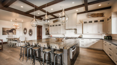 A modern kitchen with a large wooden island, bar stools, and stylish lighting, featuring white cabinets and rustic decor.